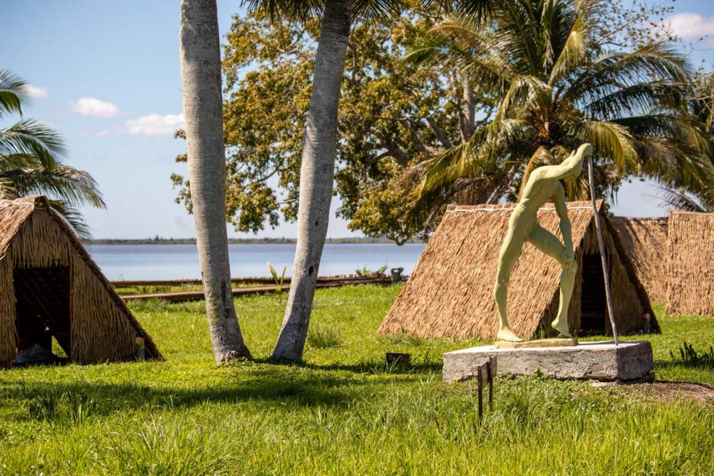 statue and small huts with thatched roofs on grass lawn